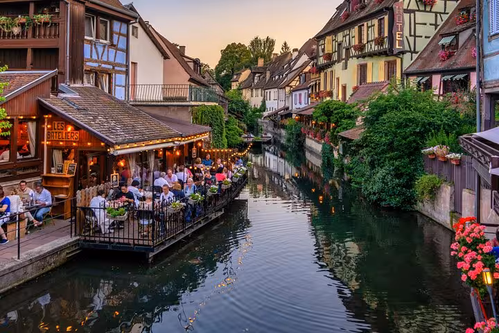 Scenic canal in Colmar's Little Venice with half-timbered houses and waterside restaurant at dusk