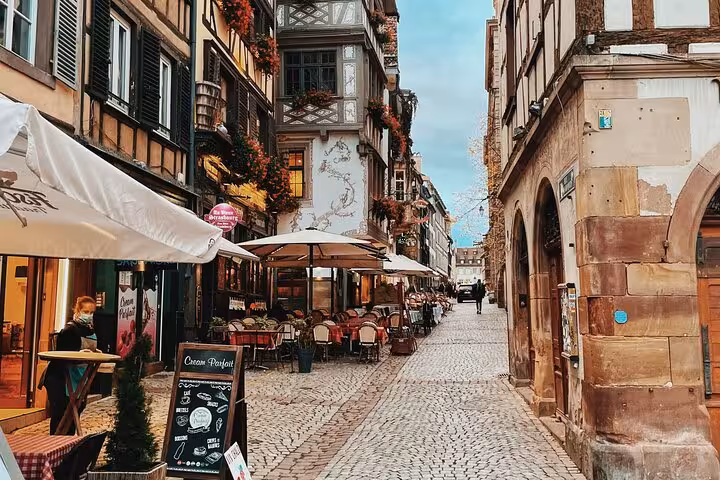Charming cobblestone street with half-timbered buildings and outdoor café terraces in Colmar, Alsace