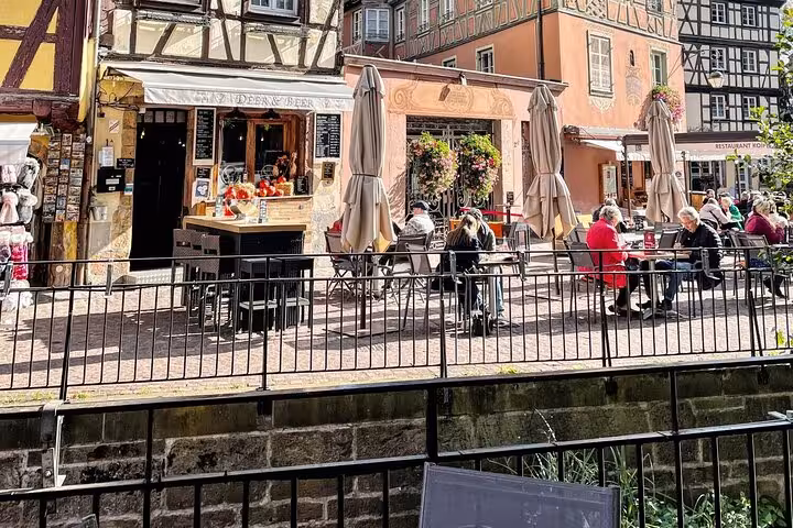 Outdoor café terrace with umbrellas beside a canal in Colmar's historic half-timbered old town