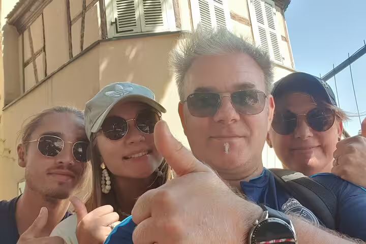Team selfie giving thumbs up on a Colmar self-guided scavenger hunt tour near historic Alsace buildings