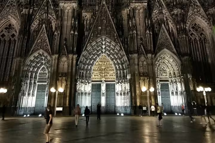 Cologne Cathedral illuminated at night with visitors exploring the gothic facade