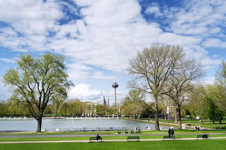 Scenic Cologne park with pond, trees, and Colonius TV tower in background on a sunny day