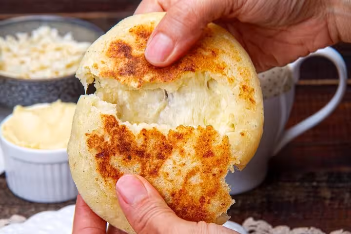 Close-up of hands breaking open a freshly made Colombian arepa with melted cheese, typical in Medellín’s street food scene.