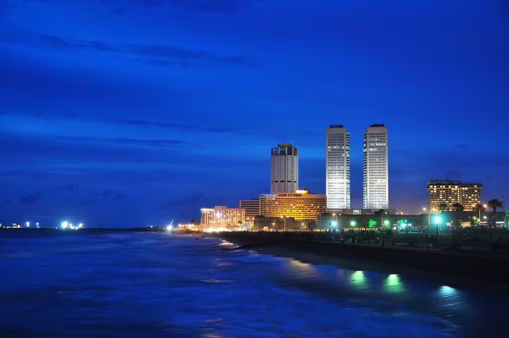 Colombo's illuminated skyline at night, with modern skyscrapers overlooking the Indian Ocean's tranquil waters.