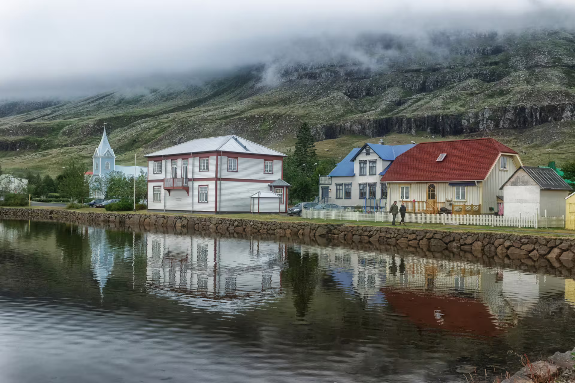 Charming Icelandic village with colorful houses reflecting on a calm lake backed by misty mountains on a 12-day Iceland grand tour.
