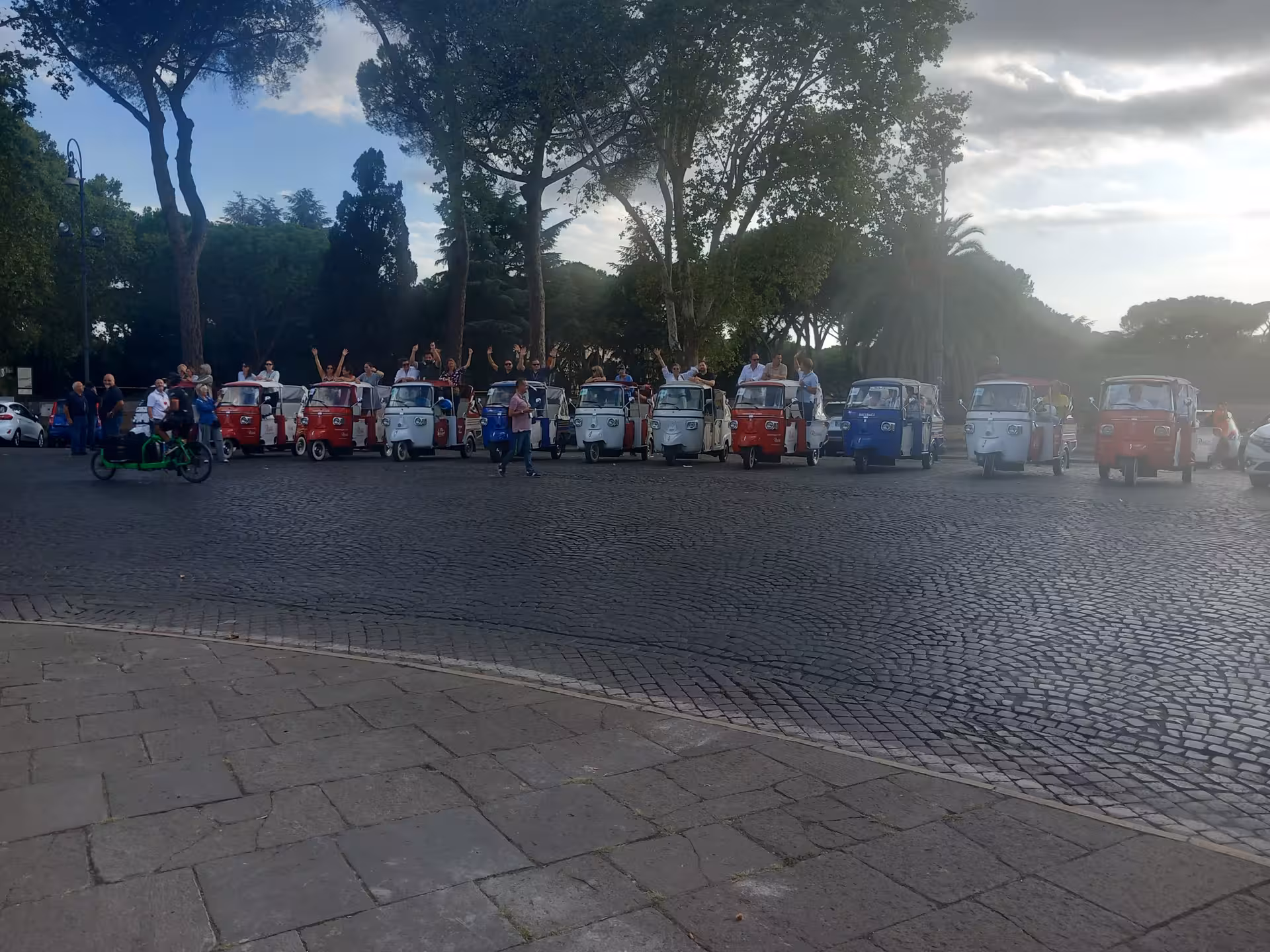 Line of colorful tuk-tuks ready for a lively Sant'Angelo Castle tour, set against Rome's lush greenery.