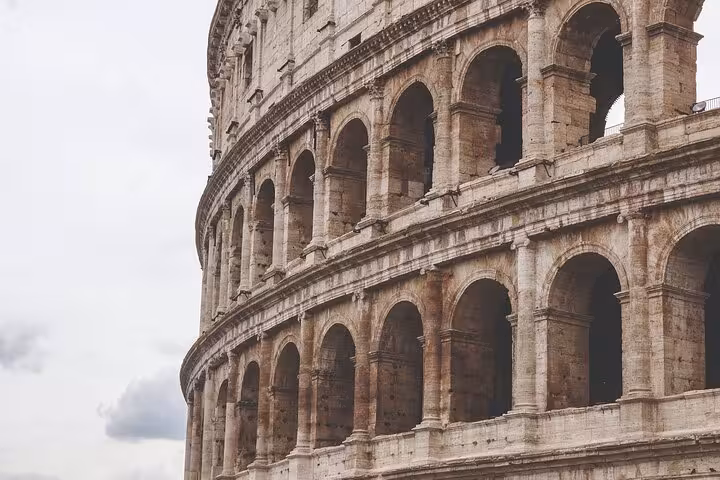 Close-up view of the Colosseum's iconic arches against a cloudy sky, highlighting Roman history on the express tour.