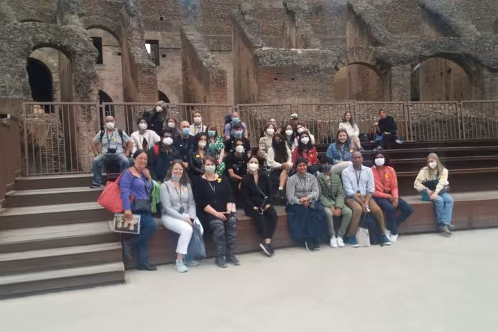 Group of tourists enjoying the Arena Floor Experience at the Colosseum with historic ruins in the background.