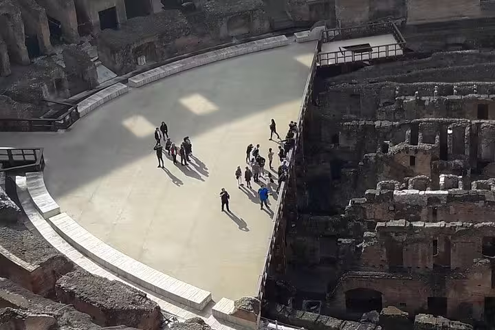Overhead view of visitors standing on the restricted Colosseum arena floor with ruins of the underground hypogeum on an exclusive tour