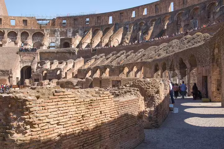 Visitors walk among ancient brick walls and arches on the Colosseum gladiators arena floor during a guided tour in Rome