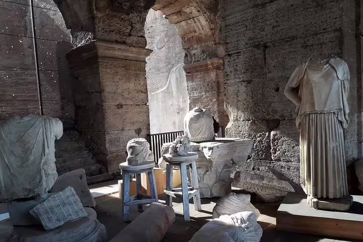 Marble statues and fragments displayed inside the Colosseum, seen on an official guided tour with Roman Forum access