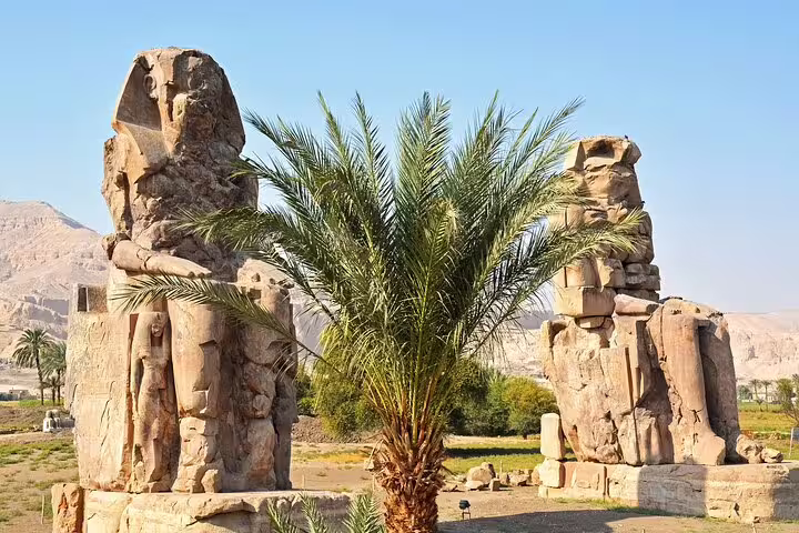 Colossi of Memnon with palm tree at Thebes, a stop on a private full-day Luxor tour from Aswan by car