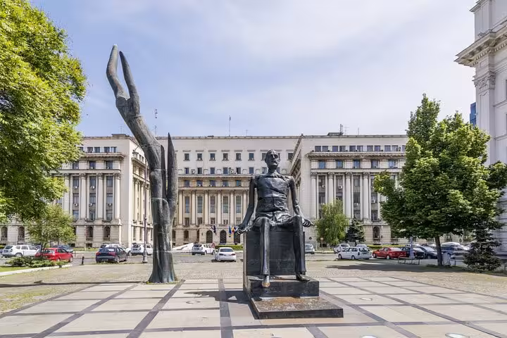 Bronze statue in Revolution Square with communist-era government building in Bucharest background