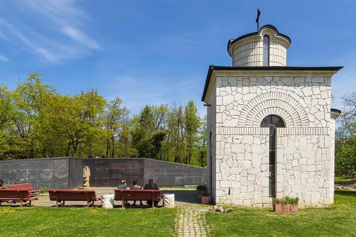Small white stone chapel with cross near communist-era memorial wall in Sofia park