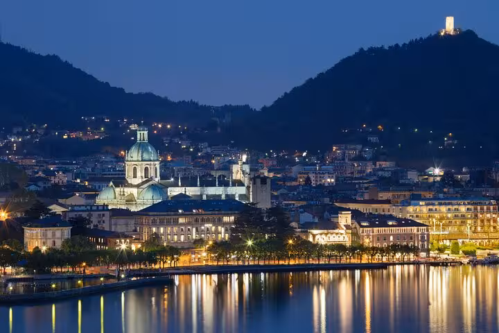 Night view of Como waterfront and Duomo reflections on Lake Como, highlight of Milan to Como Bellagio cruise tour