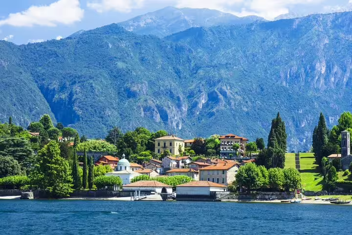 Scenic lakeside village of Como with terracotta-roofed buildings, lush trees, and Alpine mountains in background