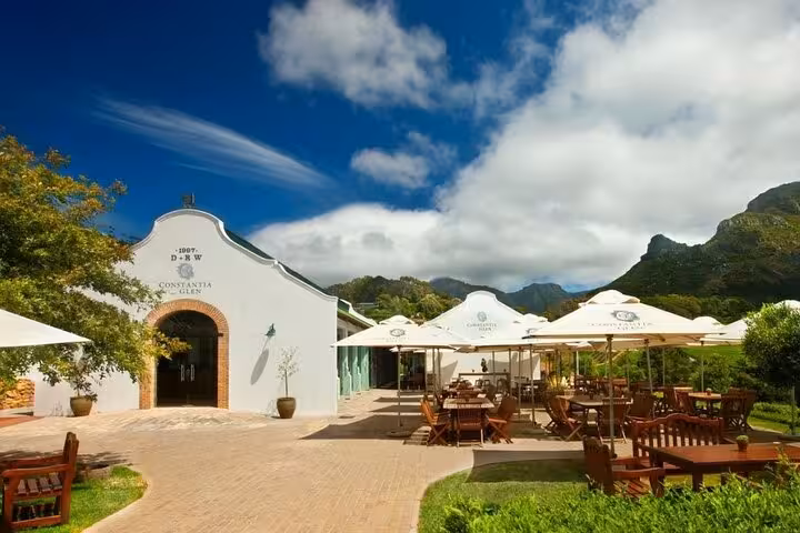 Scenic view of Constantia Glen winery courtyard with tables and umbrellas set against a backdrop of mountains and blue sky.