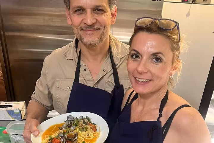 Guests in aprons holding seafood pasta with clams during a cooking workshop with a local chef in Marseille