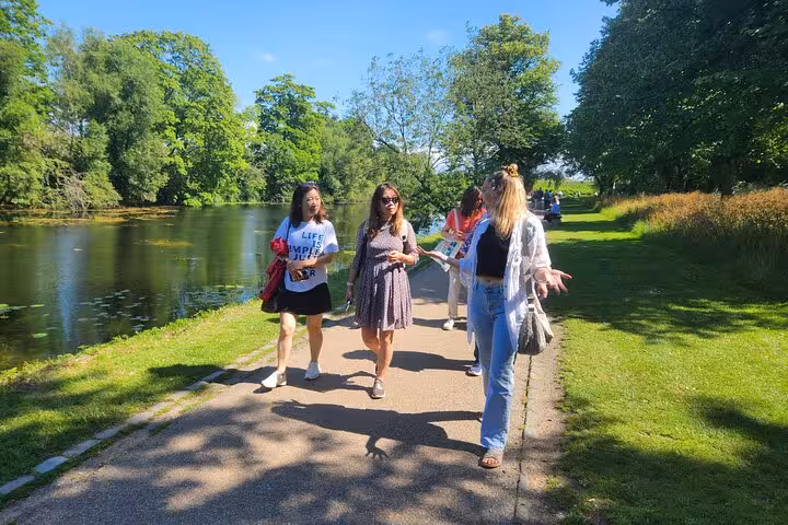 Tourists enjoying a scenic walk along a lush, tree-lined path by the water in Copenhagen, perfect for sightseeing.