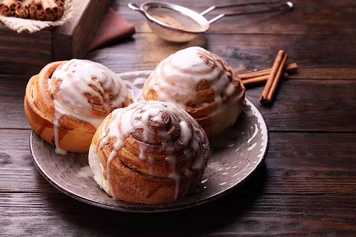 Three freshly baked cinnamon rolls with icing on a rustic plate, highlighting Copenhagen's culinary delights on a private walking tour.