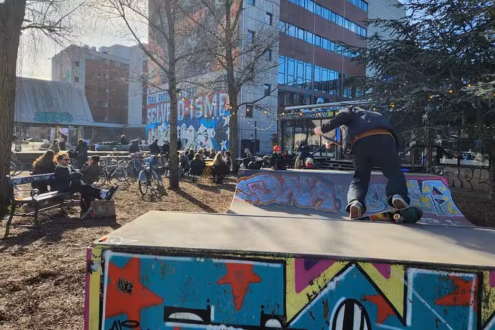 Vibrant Copenhagen skate park with locals enjoying street art and outdoor seating on a sunny day.