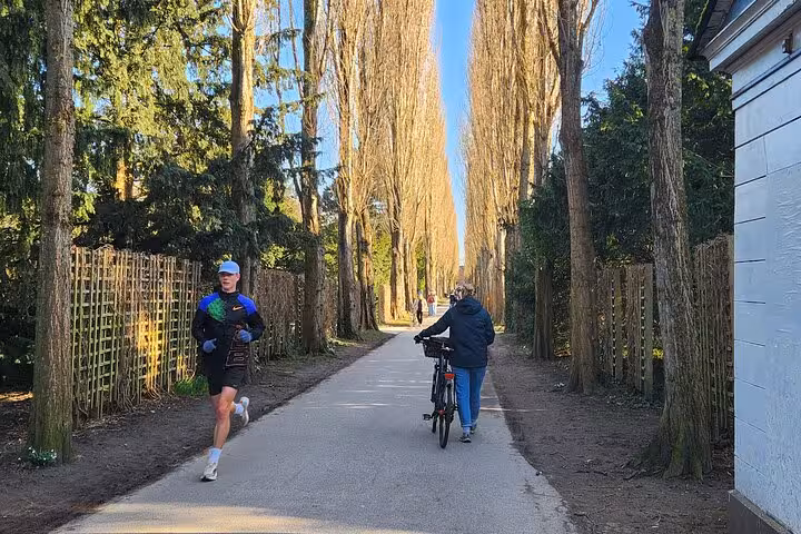 Jogger and cyclist on a tree-lined path in Copenhagen, showcasing local outdoor activities on a walking tour.