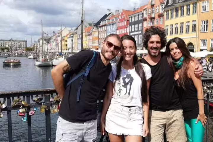 Group of friends enjoying a sunny day at Nyhavn Harbor in Copenhagen, surrounded by colorful buildings and boats.