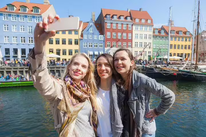 Tourists taking a selfie at Nyhavn, Copenhagen with colorful historic buildings and boats, perfect for a private walking tour adventure.