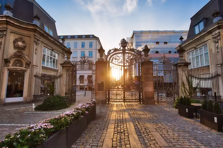 Ornate iron gate at sunset in Copenhagen's historic courtyard with cobblestone path and flowers