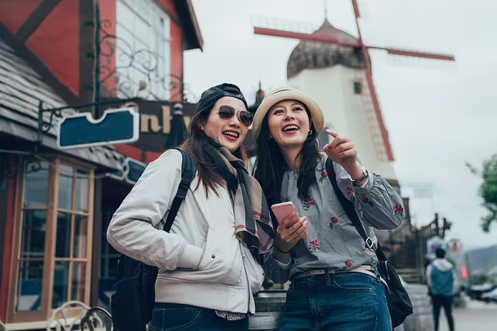 Two tourists enjoy a private full day tour in Copenhagen, exploring charming streets with a traditional windmill backdrop.