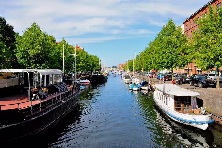 Scenic view of vibrant canal with boats and lush greenery in Copenhagen's Vesterbro and Christianshavn neighborhoods.
