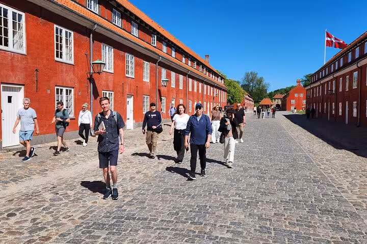 Tour group walking along cobblestone street in Copenhagen with vibrant red historic buildings and Danish flag.
