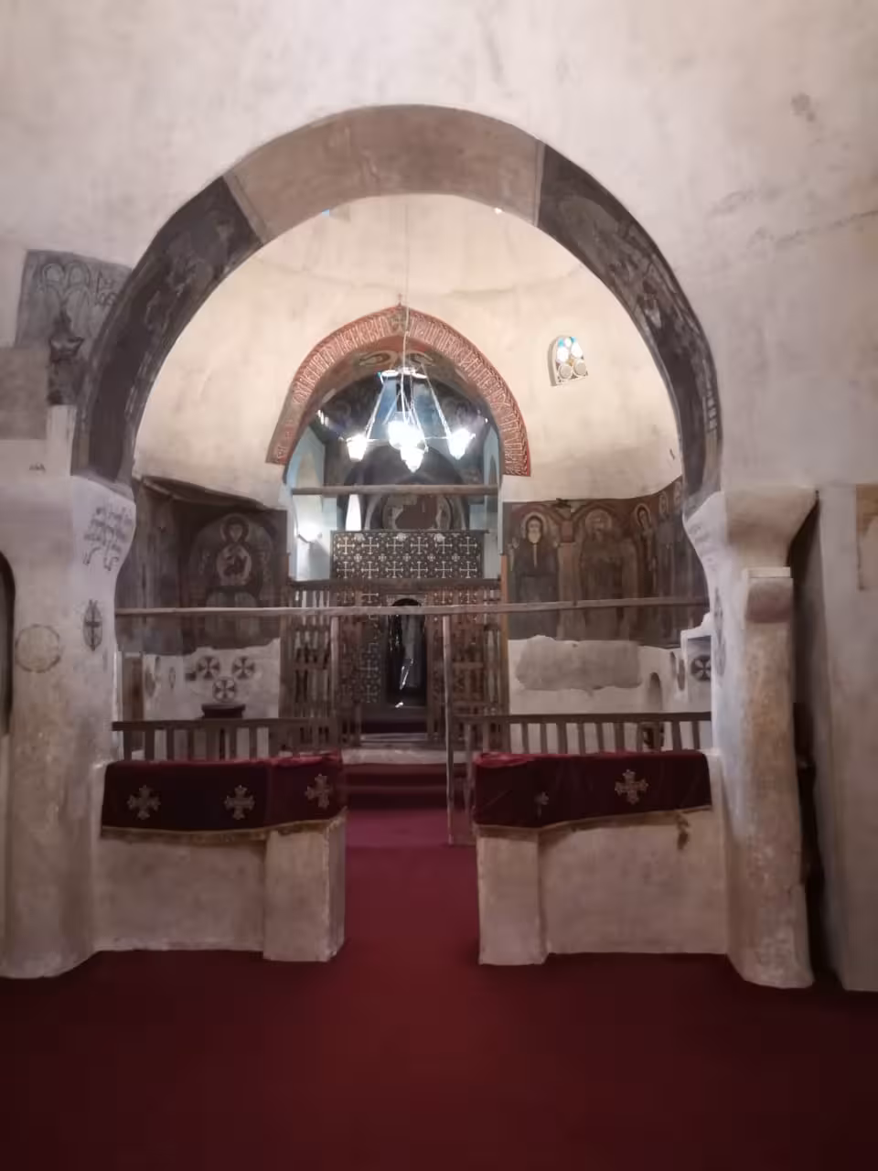 Ancient Coptic church interior with stone arches, frescoes, and ornate wooden iconostasis at Red Sea monastery