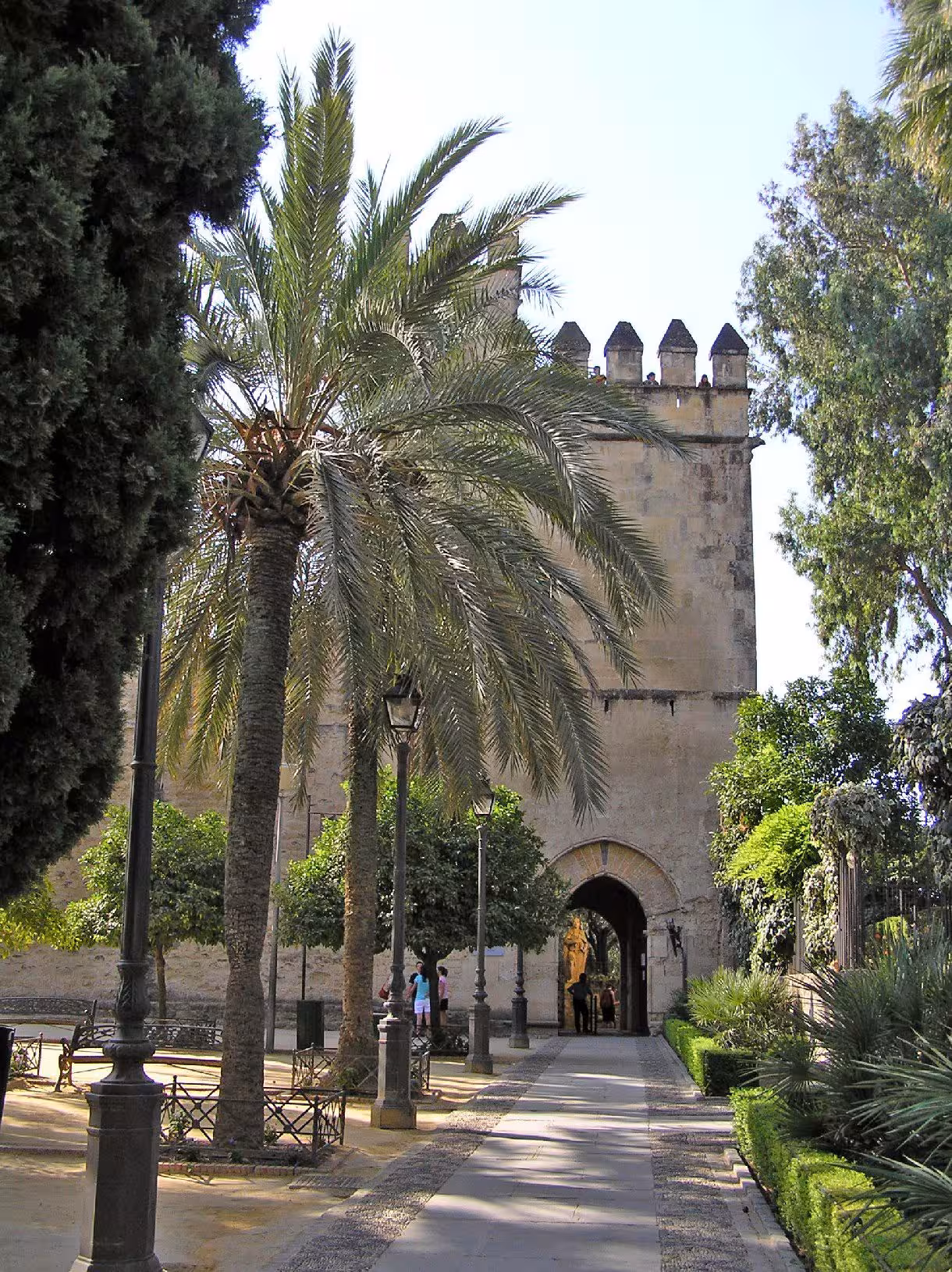 Scenic view of Córdoba's Alcázar entrance surrounded by lush gardens and palm trees, ideal for cultural exploration.