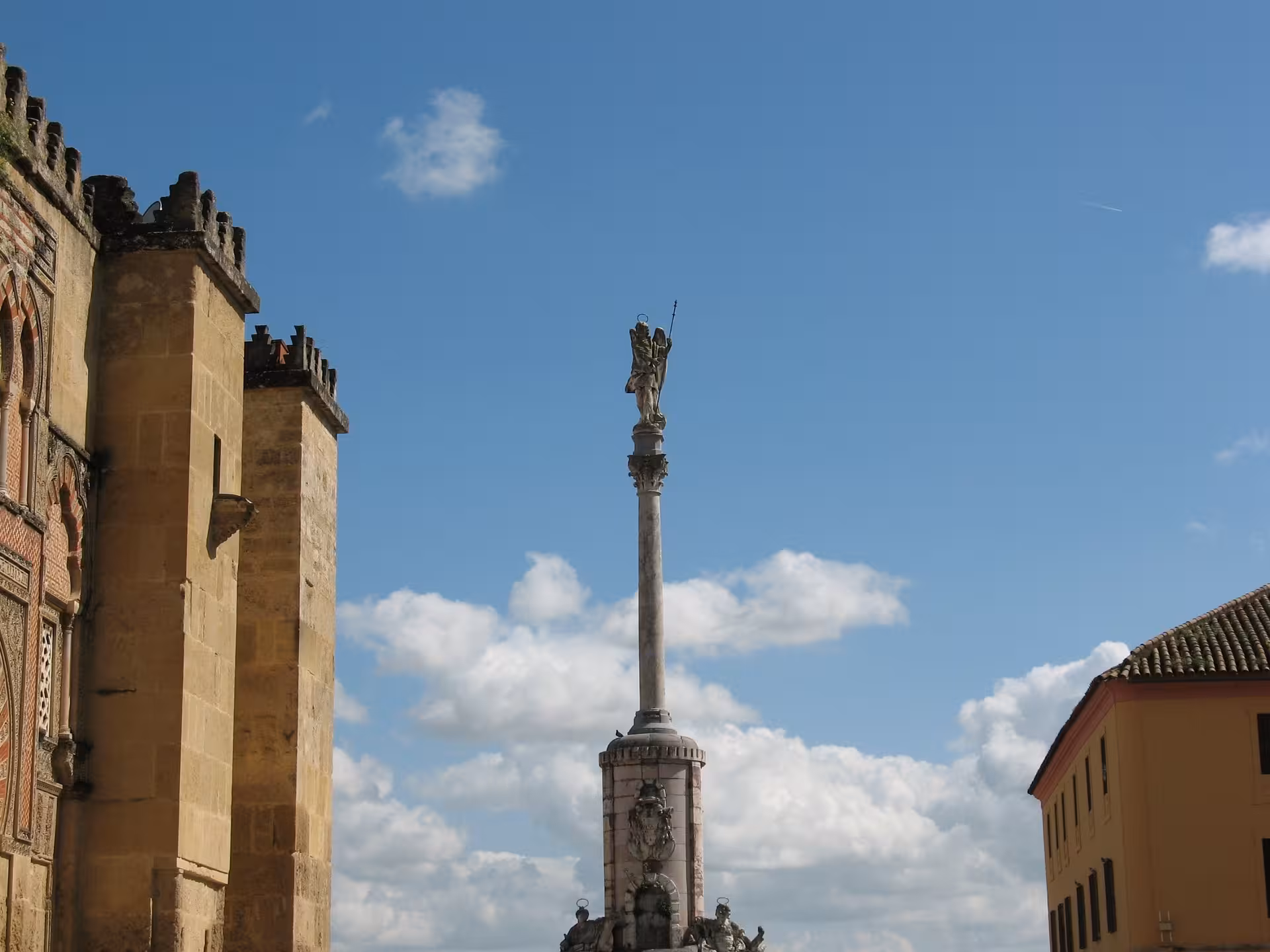 View of the Cathedral Mosque's ornate walls and a towering statue under a clear blue sky in Córdoba.