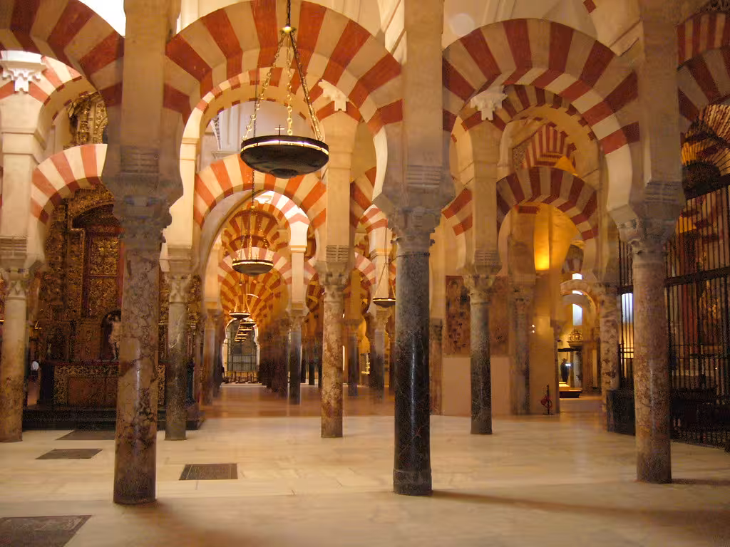 Interior of Córdoba's Mezquita showcasing iconic arches and columns with intricate red and white designs.