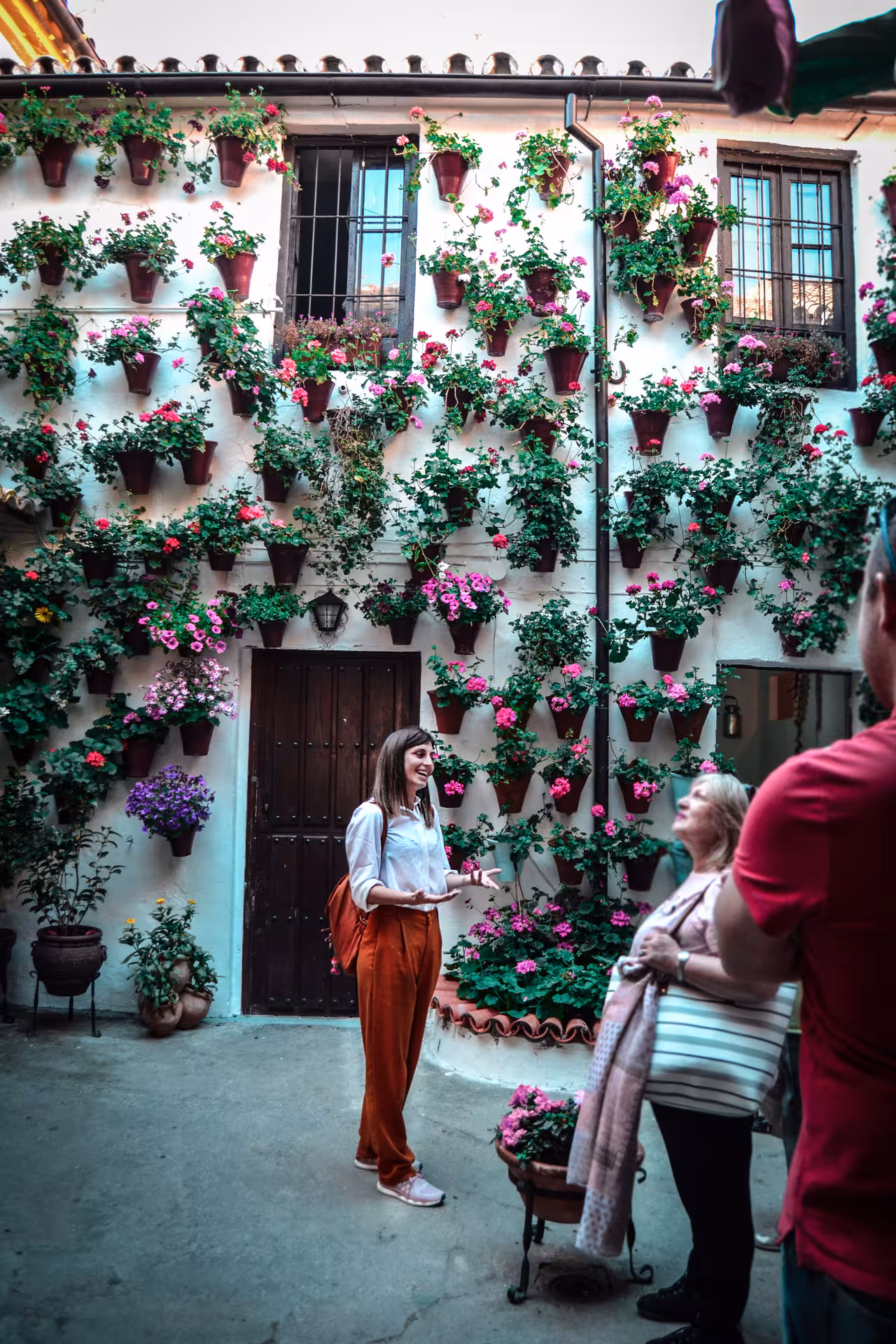 Tourists enjoying a guided tour of Córdoba's flower-filled patio, showcasing colorful blooms.