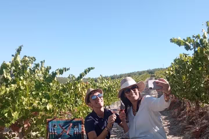 Two travelers taking a selfie and enjoying wine amidst lush vineyards in Cordoba, perfect for a convertible car tour.