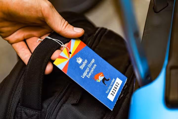 Hand attaching luggage storage tag to backpack near Corfu Port, secure bag drop service for cruise travelers