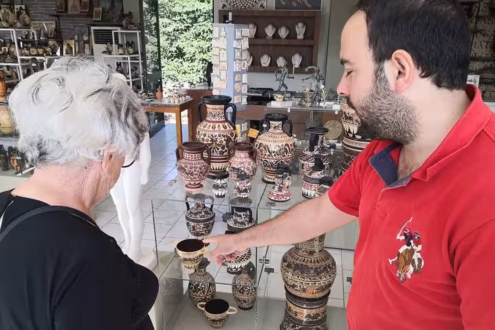 Traveler browsing handmade Greek pottery with artisan during Corinth Canal day trip from Athens workshop and tasting