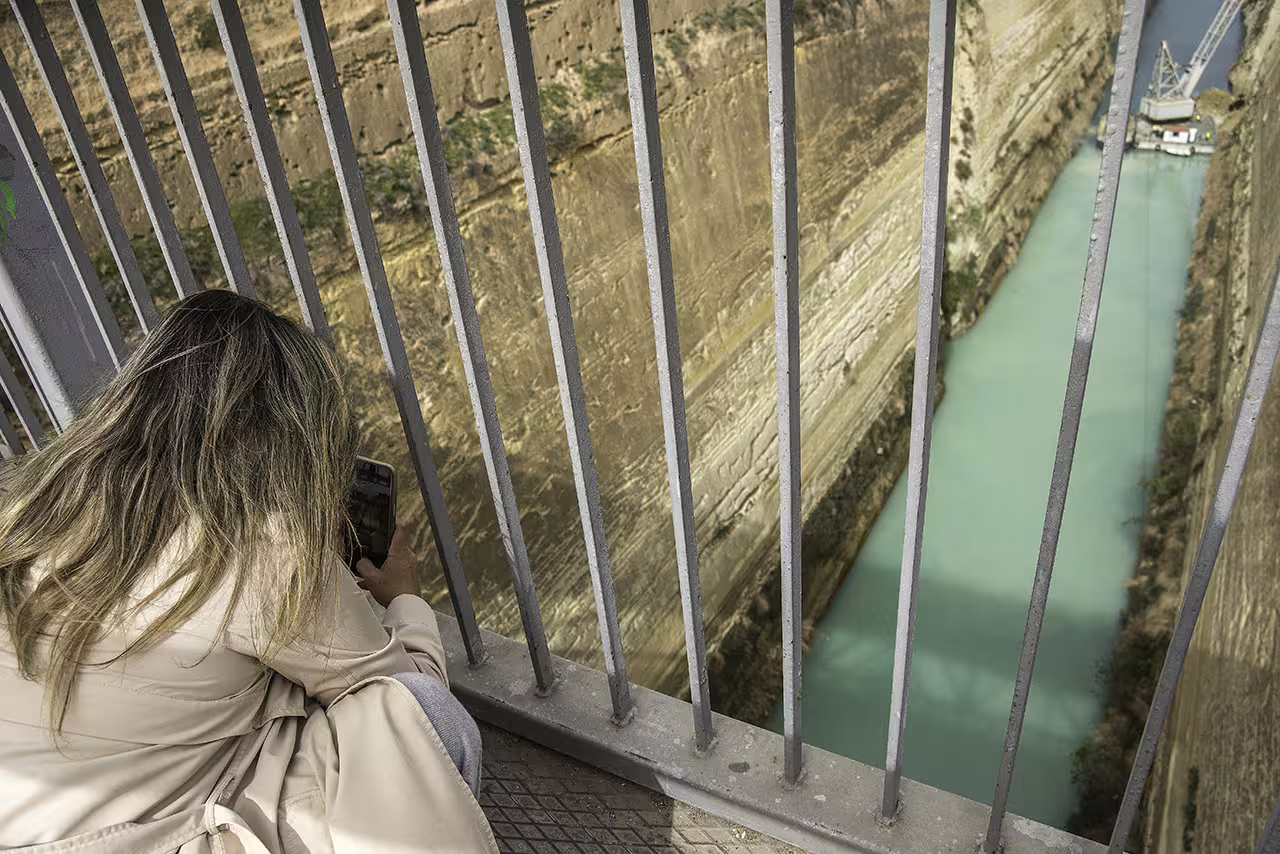 Traveler photographing the Corinth Canal from the bridge viewpoint on an Ancient Corinth and Nafplion day trip