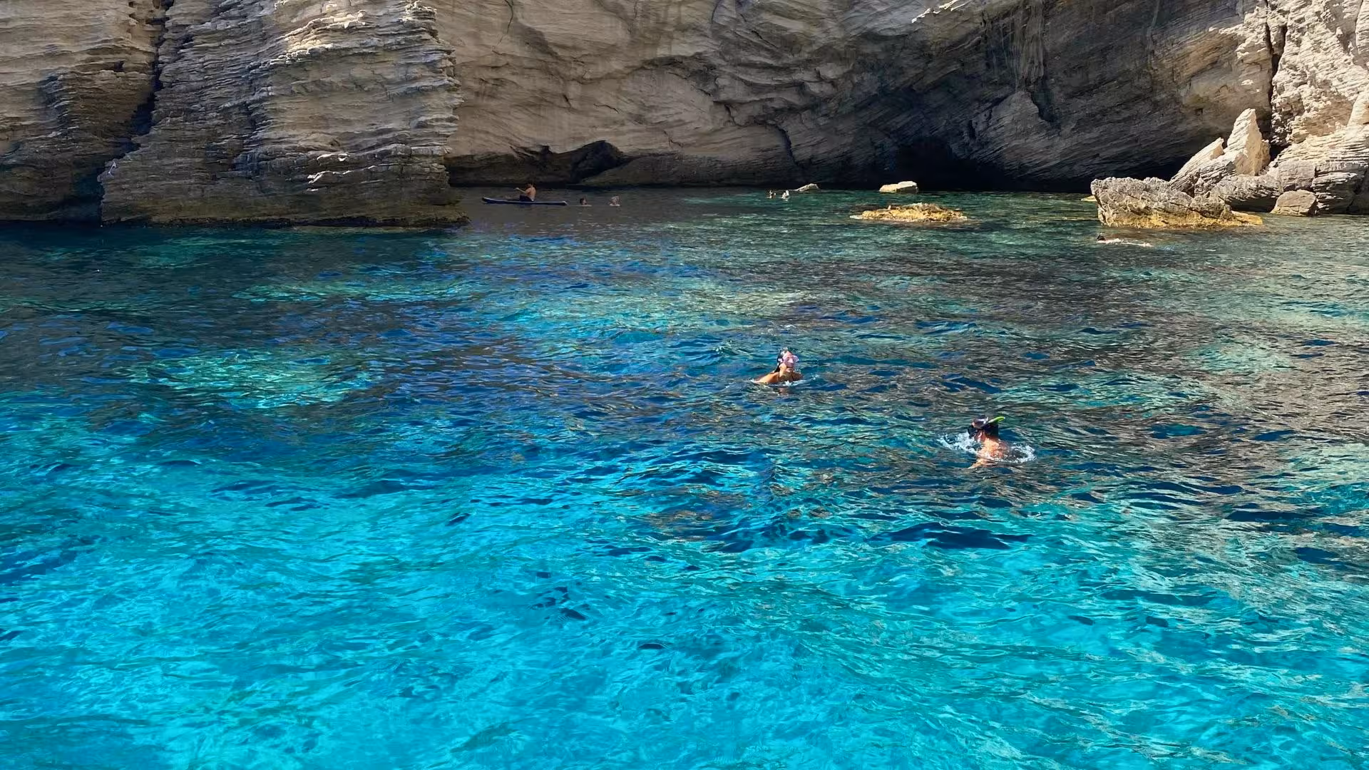 Swimmers snorkeling in the crystal-clear waters of a secluded cove in southern Corsica, surrounded by rocky cliffs.