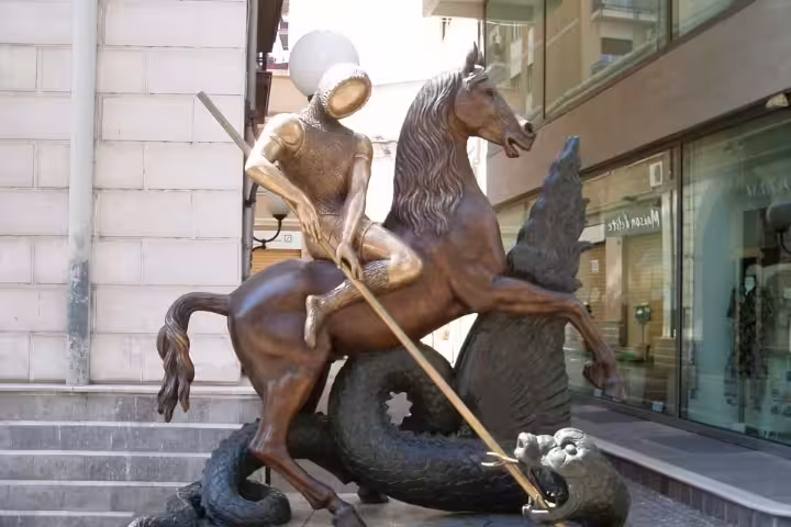 Modern bronze statue of an armored knight on horseback slaying a dragon in central Cosenza, symbol of local legends and art