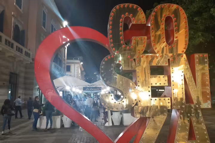 Night view of illuminated Cosenza heart sculpture on lively street, a romantic stop on Byzantines and Normans tour in Calabria
