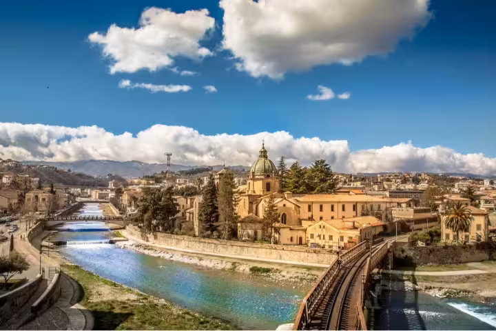 Panoramic view of Cosenza, Italy with historic riverside buildings, church dome, bridge and mountains on a 3-day city break