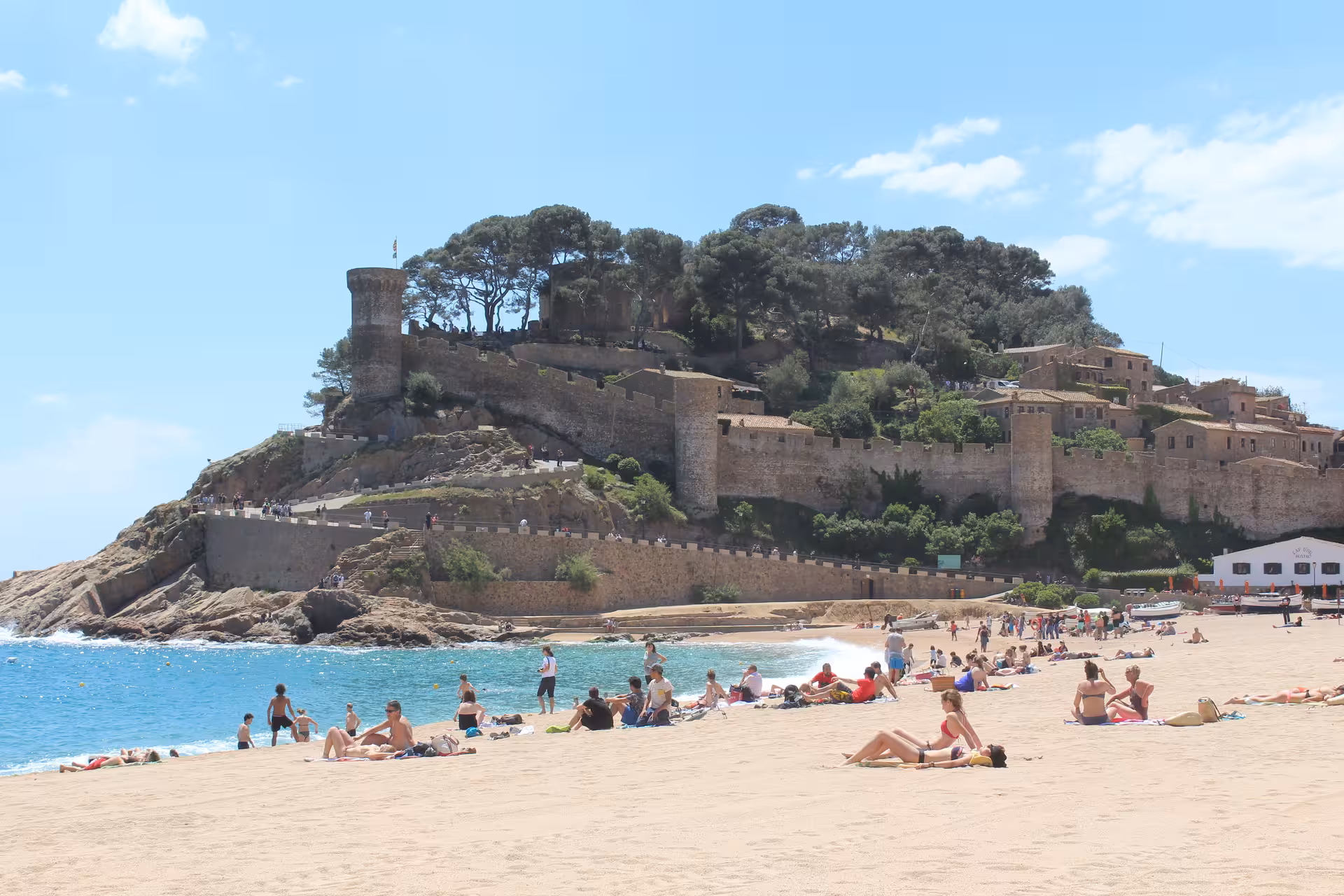 Sunbathers on a wide Costa Brava beach with Tossa de Mar fortress, day tour from Barcelona