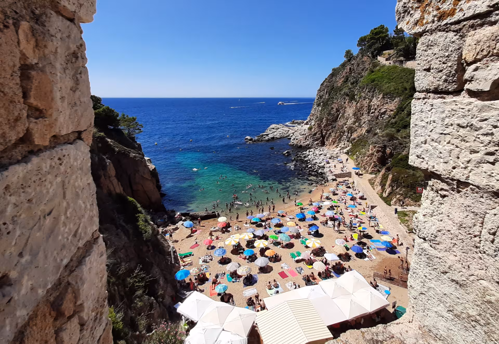 Clifftop view of a Costa Brava cove with turquoise water and umbrellas, Barcelona day trip beach escape