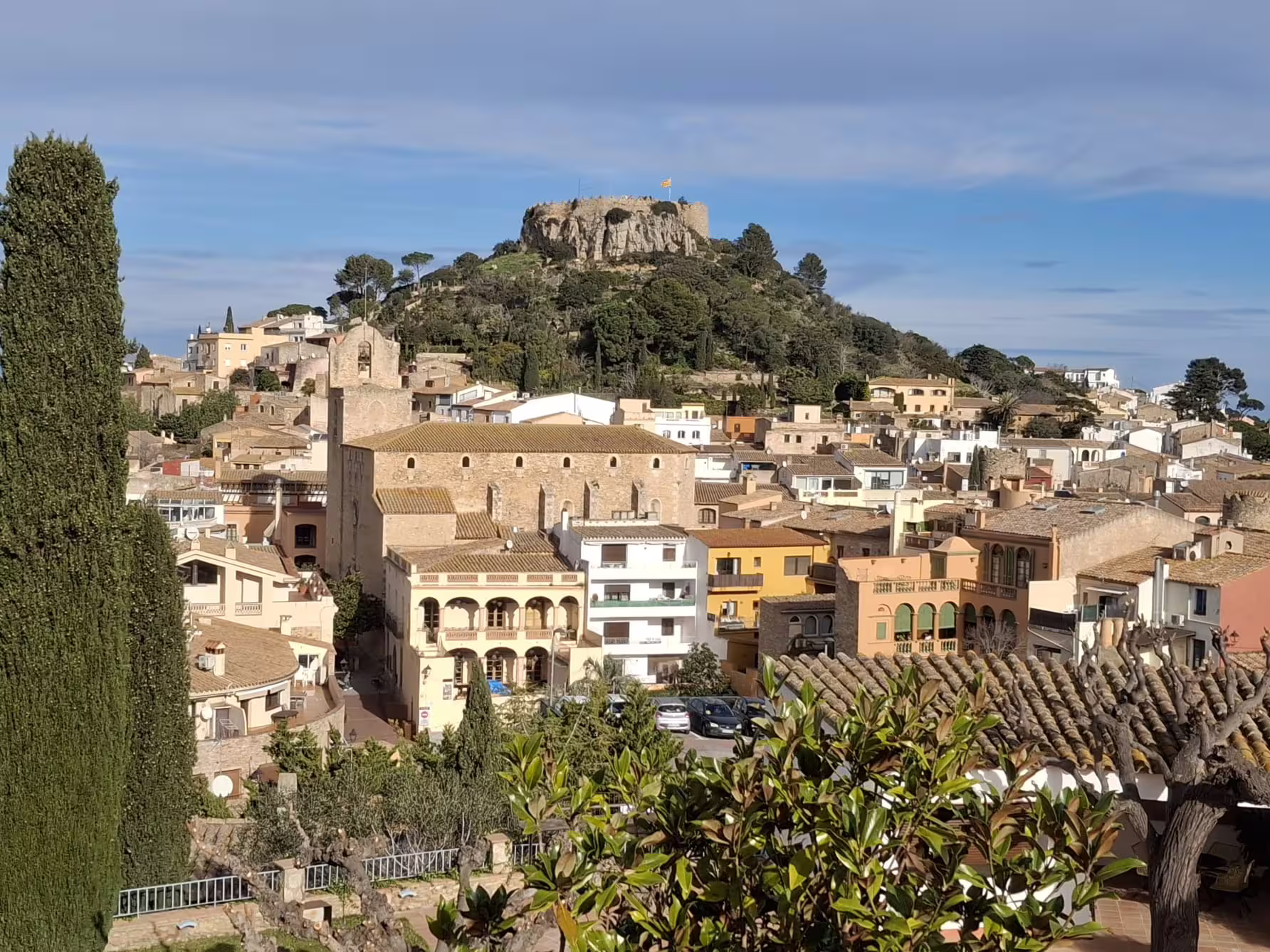 Charming medieval town in Costa Brava with rustic architecture and a hilltop castle under a clear blue sky.