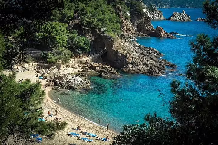 Scenic beach surrounded by lush greenery and rocky cliffs on Costa Brava, ideal for a relaxing seaside escape.