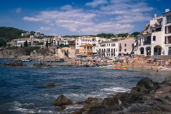 Sunny Costa Brava beach with vibrant umbrellas and scenic Mediterranean coastline, perfect for a Dalí Museum tour stop.